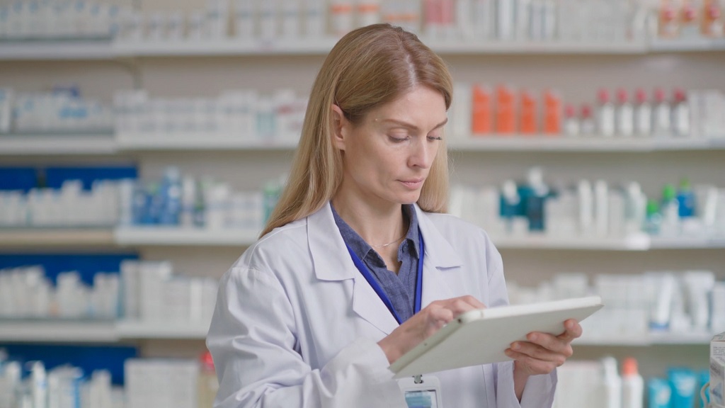 Farmaceutkinja u apoteci proverava recept na tabletu, ilustracija kako se ostvaruje pravo na besplatne lekove u ovlašćenim apotekama
