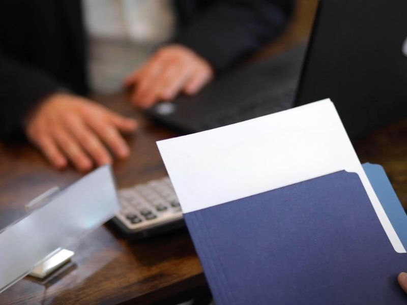 Čovek drži fasciklu u ruci plave boje i stoji u agenciji agenta za registraciju firme