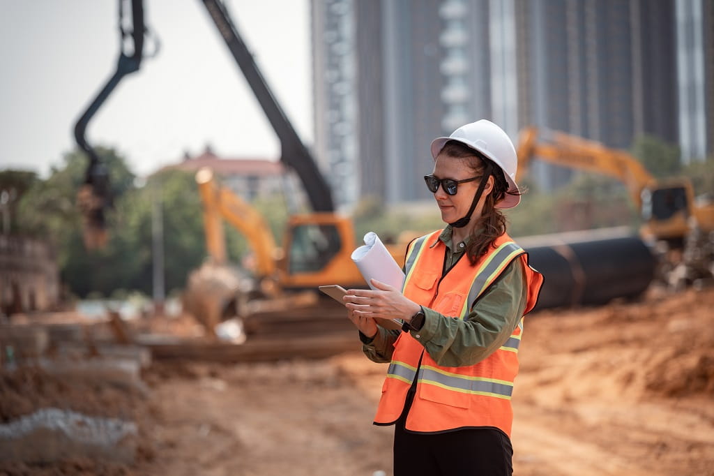 Inženjer na gradilištu sa zaštitnom opremom proverava planove i mobilni uređaj