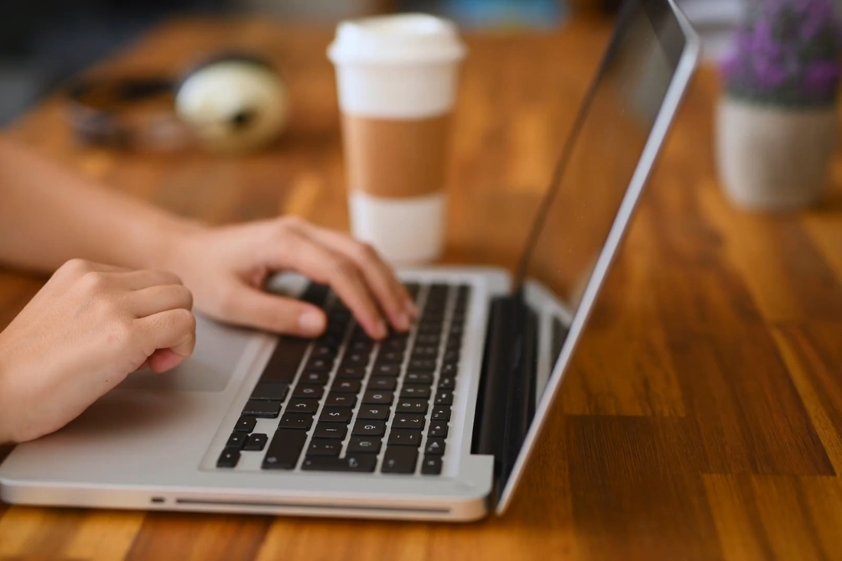 devojka koristi laptop, pored nje kafa za poneti