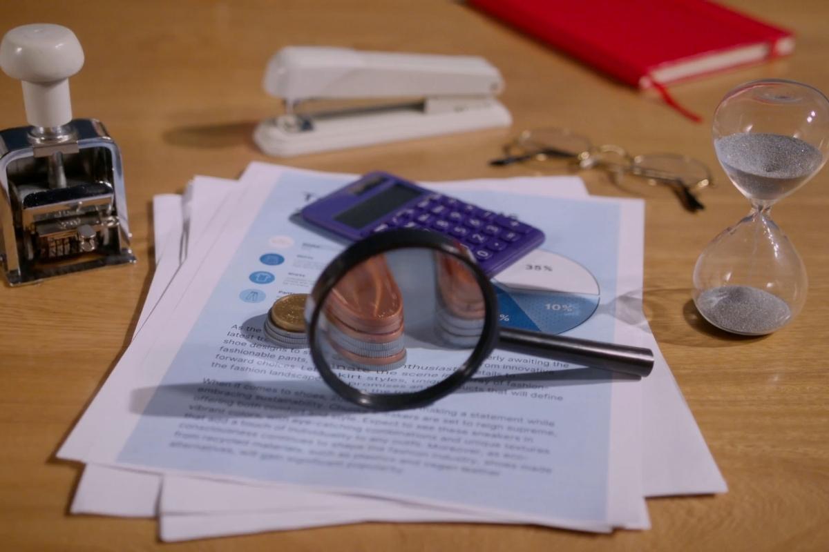 Kancelarijski sto sa dokumentima, kalkulatorom, pečatom, lupom, peščanim satom i ključevima, simbol analize finansija i naplate potraživanja.