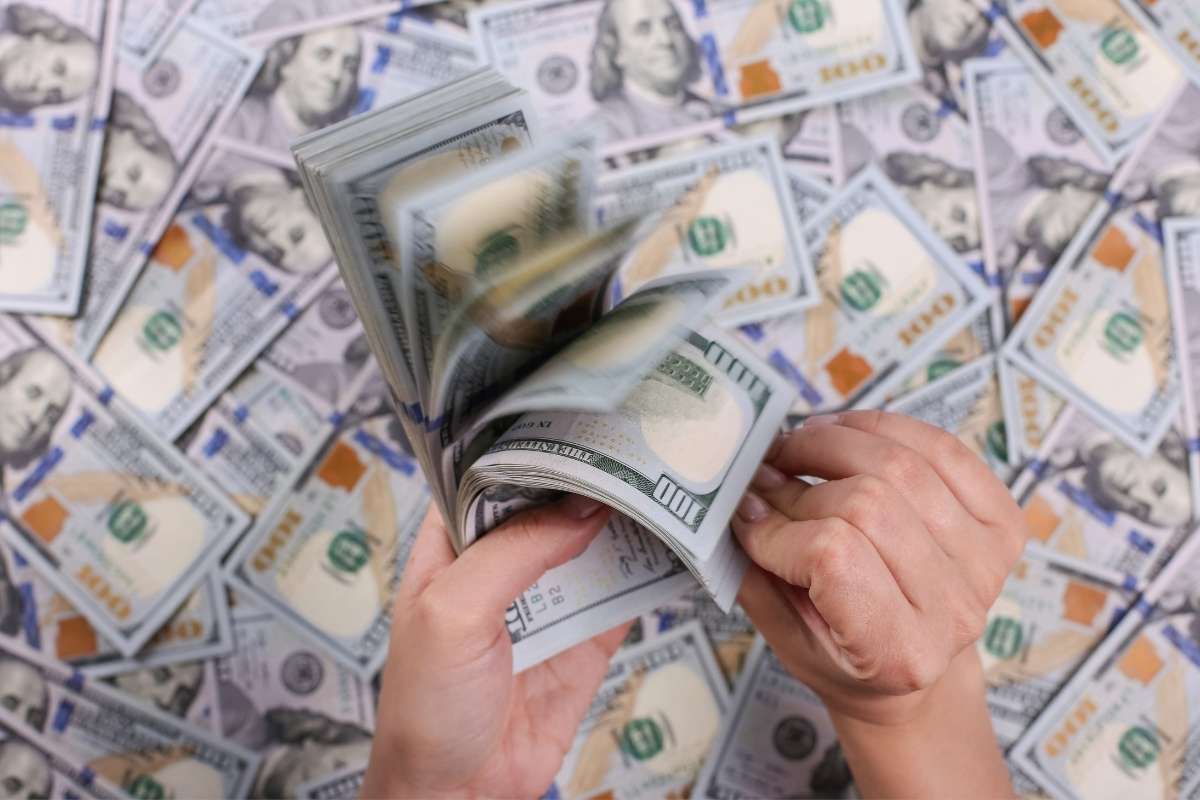 osoba drži veliku svotu novca u rukama i na stolu takođe mnogo novca
